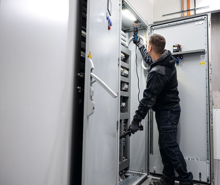 Osoba v bezpečnostním vybavení testuje elektrický panel pomocí zkoušečky napětí.