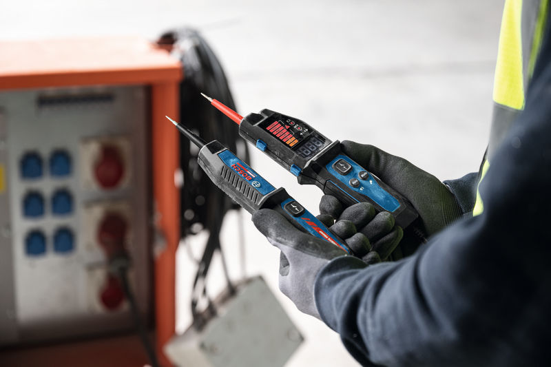 Osoba v bezpečnostním vybavení používá zkoušečku napětí poblíž elektrického rozvaděče.