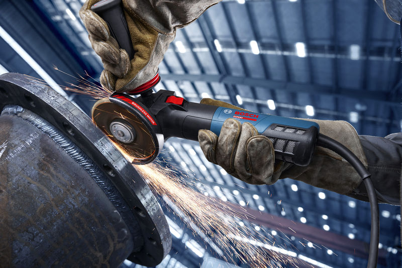 Osoba v bezpečnostním vybavení brousí kov úhlovou bruskou a vytváří jiskry.
