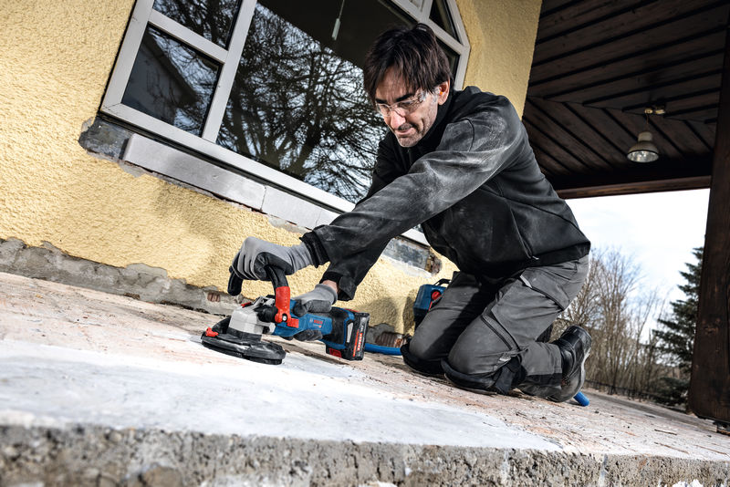 Osoba v bezpečnostním vybavení brousí betonový povrch elektrickým nářadím.