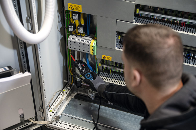 Osoba v bezpečnostním vybavení používá zkoušečku napětí na elektrickém rozvaděči.