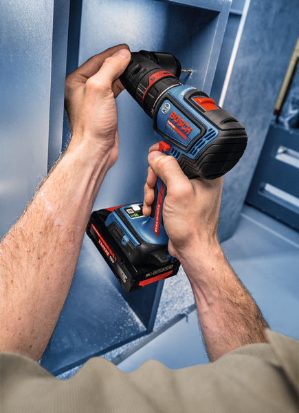 Osoba používá akumulátorovou vrtačku k sestavení modré kovové police.