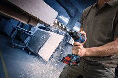 Osoba vrtá do dřeva akumulátorovou vrtačkou, létající dřevěné hobliny.